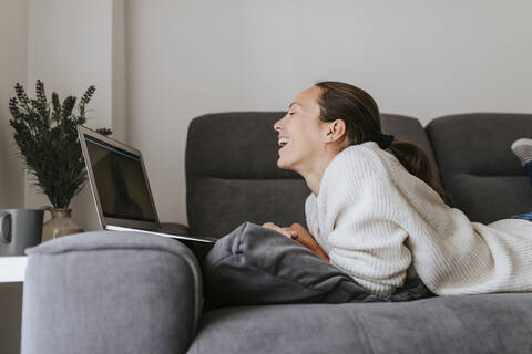 Woman laughing while talking to friend through video call on laptop at home stock photo