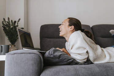 Woman laughing while talking to friend through video call on laptop at home - DMGF00329