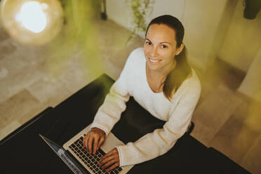 Lächelnde Frau sitzt mit Laptop an der Kücheninsel - DMGF00343