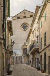 Spanien, Mallorca, Pollenca, Leere Gasse zwischen alten Stadthäusern mit Kirche im Hintergrund - JMF00543