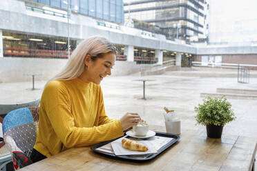 Glückliche junge Frau beim Frühstück im Café während der Regenzeit - IFRF00094