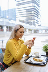 Young woman using mobile phone at cafe during rainy season - IFRF00095