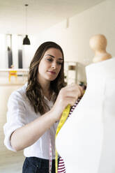 Beautiful female designer measuring fabric on mannequin at studio - GIOF09774