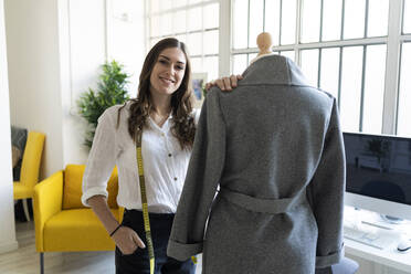Smiling fashion designer standing by mannequin in studio - GIOF09780