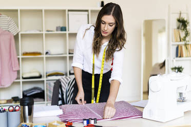 Young creative designer measuring fabric kept on desk at studio - GIOF09785