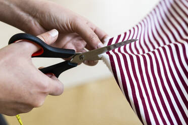 Female designer's hand cutting fabric in studio - GIOF09788