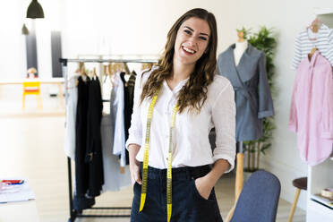 Female designer smiling with hands in pockets while standing in studio - GIOF09791