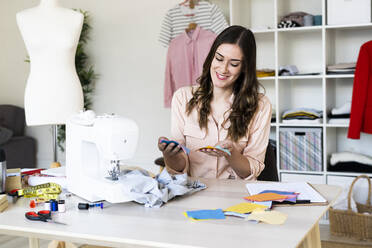 Smiling female designer analyzing fabric swatches while sitting in studio - GIOF09800