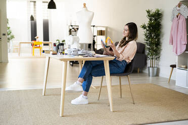 Schneiderin prüft Stoffmuster, während sie auf einem Stuhl im Atelier sitzt - GIOF09802