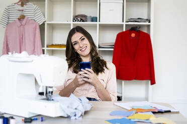 Young female designer holding smart phone in studio - GIOF09804