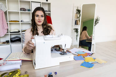 Smiling female creative tailor sitting with sewing on machine at studio - GIOF09808