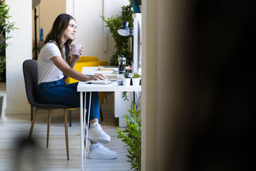 Geschäftsfrau, die einen Computer benutzt und eine Kaffeetasse im Büro hält - GIOF09816