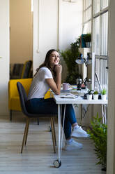 Junge Geschäftsfrau mit Hand am Kinn im Büro sitzend - GIOF09822