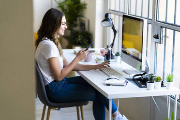 Lächelnde Geschäftsfrau, die ein Smartphone benutzt, während sie im Büro sitzt - GIOF09823