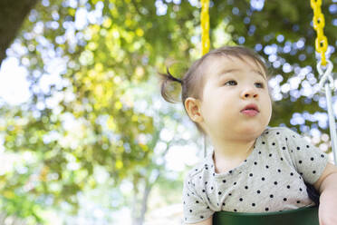 Thoughtful Toddler Girl Sits in Outdoor Swing Looking to the Side - CAVF91151