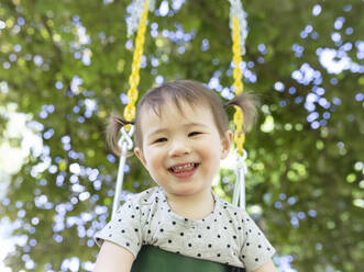Happy Smiling Toddler Girl with Pigtails Swings Outdoors Under A Tree - CAVF91152
