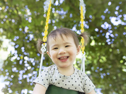 Happy Smiling Kleinkind Mädchen mit Zöpfen Swings im Freien unter einem Baum - CAVF91152
