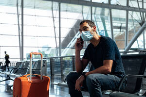 Young man wearing a face mask talking on the phone at the airport - CAVF91206