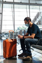 Junger Mann mit Gesichtsmaske schaut auf sein Handy am Flughafen - CAVF91207