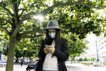 Young woman with a mask using her mobile phone in the city - CAVF91238