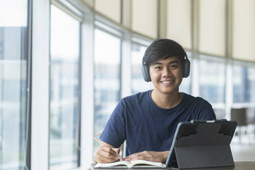 Junger Collegestudent mit Computer und mobilem Gerät beim Lernen - CAVF91249