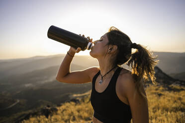 Nahaufnahme einer jungen Sportlerin, die Wasser aus einer Flasche trinkt - CAVF91257