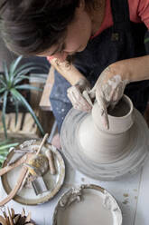 Young woman working clay in ceramic studio from above - CAVF91269