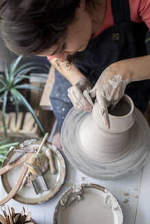 Young woman working clay in ceramic studio from above - CAVF91269