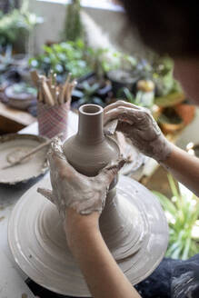 Backlit close-up of hands working on ceramic pot - CAVF91271