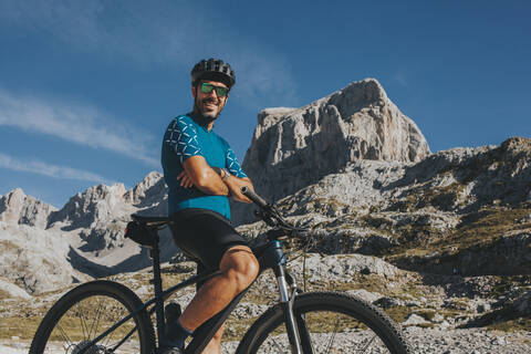 Lächelnder Mountainbiker mit verschränkten Armen im Nationalpark Picos de Europa in Kantabrien, Spanien, lizenzfreies Stockfoto