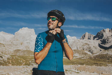 Cyclist adjusting cycling helmet at Picos de Europa National Park on sunny day, Cantabria, Spain - DMGF00355