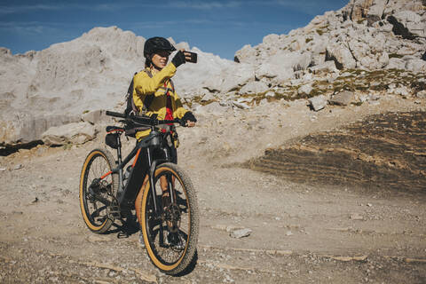 Female cyclist photographing at Picos de Europa National Park on sunny day, Cantabria, Spain stock photo