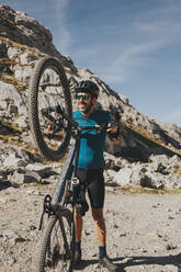 Verspielter männlicher Radfahrer mit Mountainbike an einem sonnigen Tag, Nationalpark Picos de Europa, Kantabrien, Spanien - DMGF00374