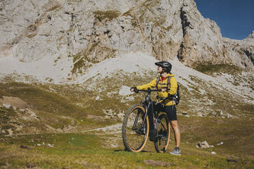 Frau mit Fahrrad, die an einem sonnigen Tag gegen einen Felsen blickt, Nationalpark Picos de Europa, Kantabrien, Spanien - DMGF00375