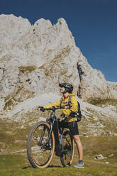 Radfahrerin mit Fahrrad vor einem Felsen im Nationalpark Picos de Europa, Kantabrien, Spanien - DMGF00376