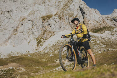 Smiling female cyclist with mountain bike on sunny day at Picos de Europa National Park, Cantabria, Spain - DMGF00377