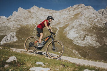 Radfahrerin beim Radfahren in der Nähe eines Felsenberges im Nationalpark Picos de Europa, Kantabrien, Spanien - DMGF00381