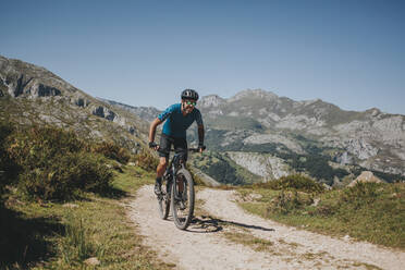 Männlicher Radfahrer fährt Mountainbike auf einem Weg gegen den Himmel, Nationalpark Picos de Europa, Asturien, Spanien - DMGF00384