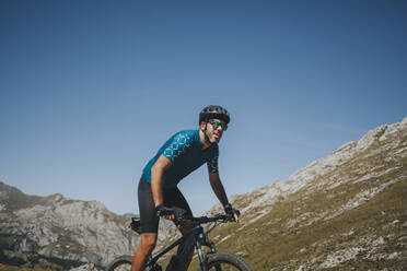 Männlicher Radfahrer fährt Mountainbike gegen den Himmel an einem sonnigen Tag, Picos de Europa National Park, Asturien, Spanien - DMGF00385