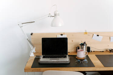 Von oben Komposition der modernen tragbaren Netbook mit schwarzem Bildschirm auf hölzernen Schreibtisch in der Nähe von Tasse und Brillen in hellen Büro platziert - ADSF18188