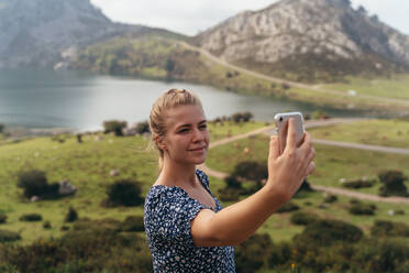 Side view of female with modern mobile phone taking selfie with amazing lush highland valley of background - ADSF18189