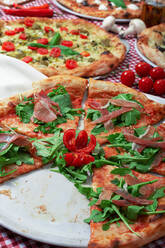 Appetizing sliced Italian pizza with Parma ham and fresh ruccola served on table with various types of pizza - ADSF18207
