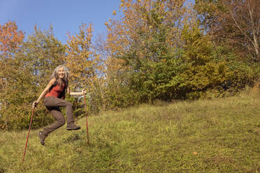 Fröhliche Frau mit Wanderstock springt auf Berg im Alpenvorland, Deutschland - FCF01907