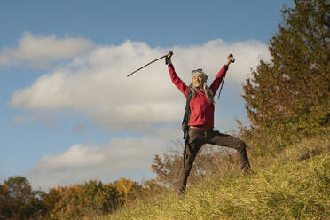 Smiling woman standing with hand raised on mountain against sky at Alpine Foothills, Germany - FCF01912