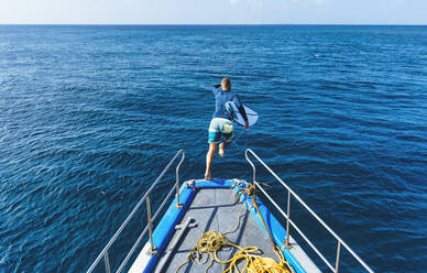 Männlicher Surfer mit Surfbrett springt vom Bootsdeck ins Meer - KNTF06013