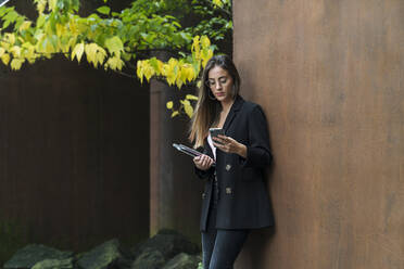 Schöne Geschäftsfrau mit Brille, die ein Mobiltelefon vor einer braunen Wand benutzt - MTBF00715