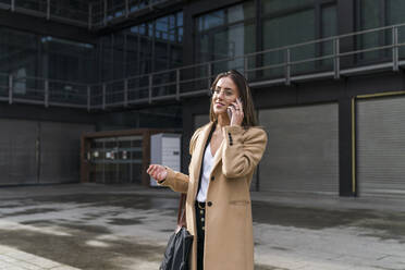 Smiling businesswoman talking on phone against office building - MTBF00721