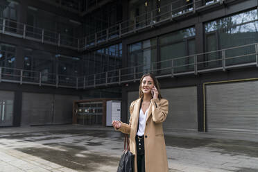 Smiling young female entrepreneur talking on phone against office building - MTBF00722