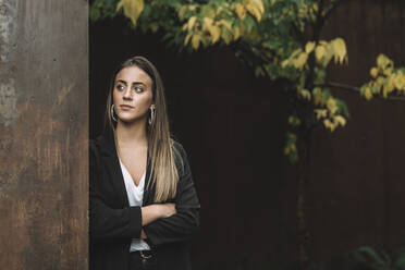 Thoughtful businesswoman with arms crossed looking away while leaning on wall - MTBF00725