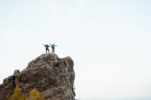 Couple with arms outstretched standing on mountain peak against sky - RCPF00403